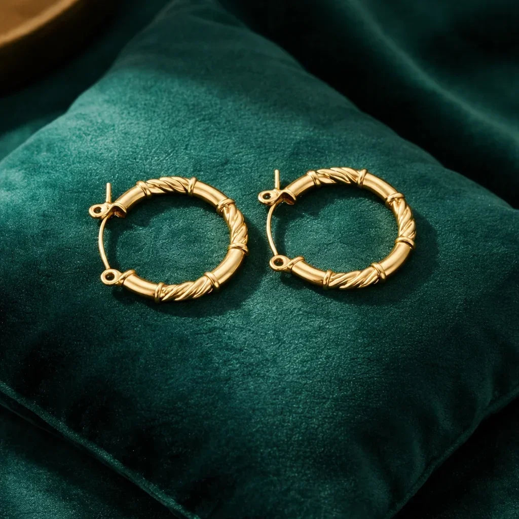 Gold twisted hoop earrings on a green velvet cushion, minimalist jewelry style