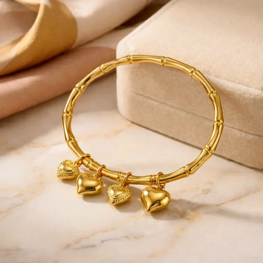 Gold bamboo-inspired bracelet with four heart-shaped charms on marble surface