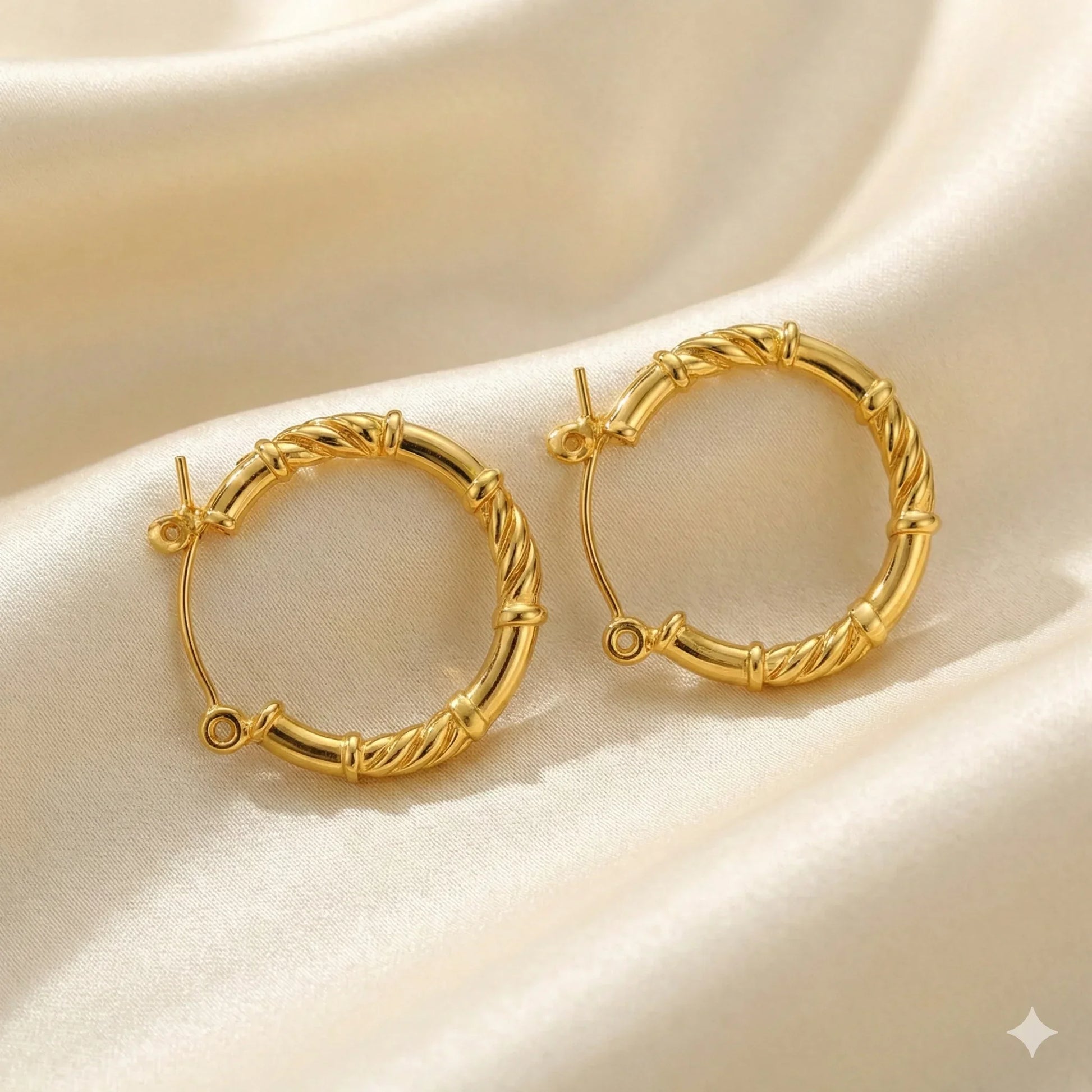 Gold twisted hoop earrings on a cream satin background, minimal and lightweight design